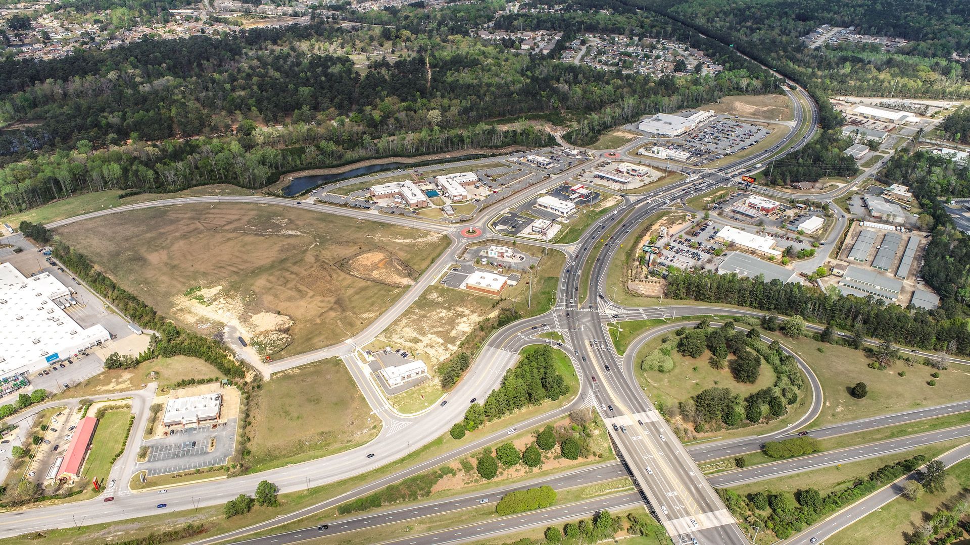 Aerial view of a highway interchange beside a suburban development and wooded hills.