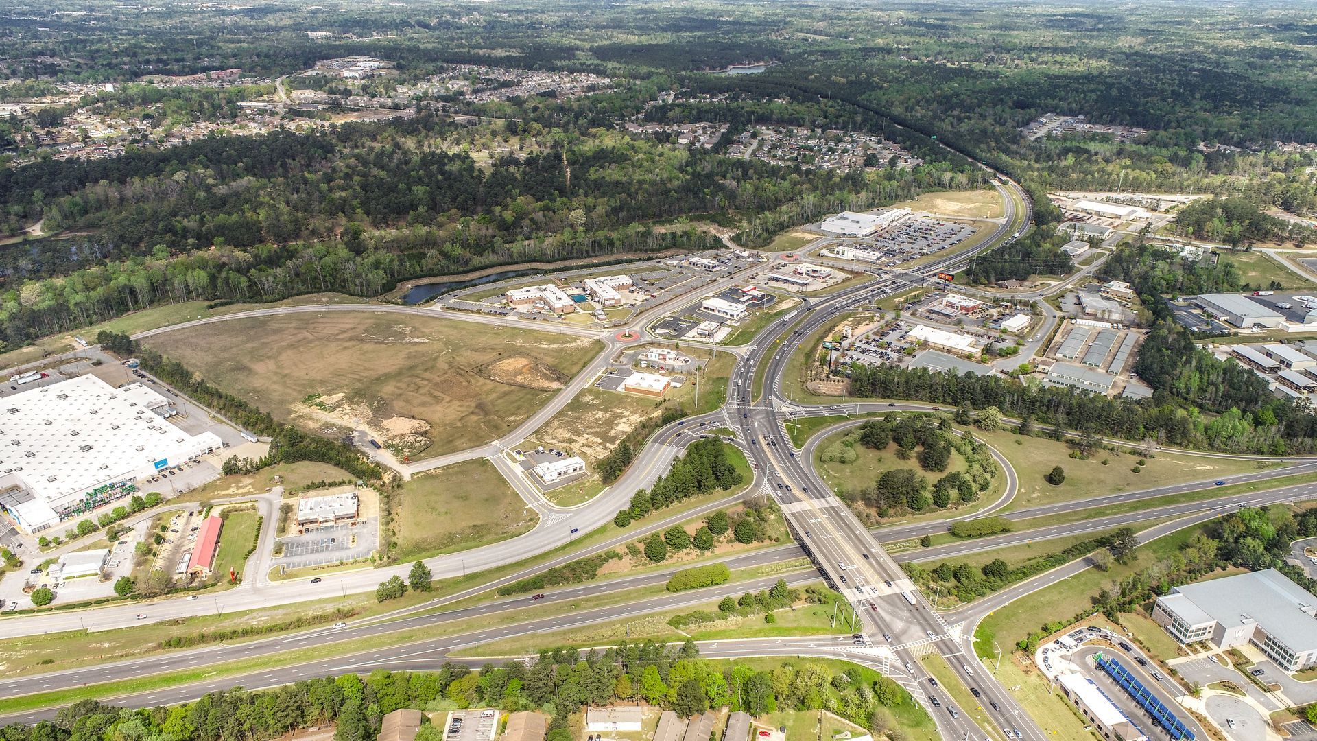 Aerial view of a suburban area with roads, buildings, trees, and a highway interchange.