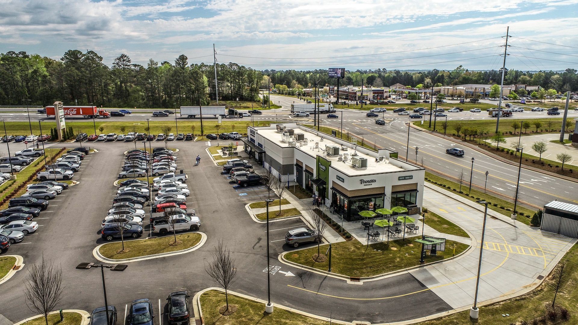 Aerial view of a parking lot and commercial buildings beside a busy road under a cloudy sky
