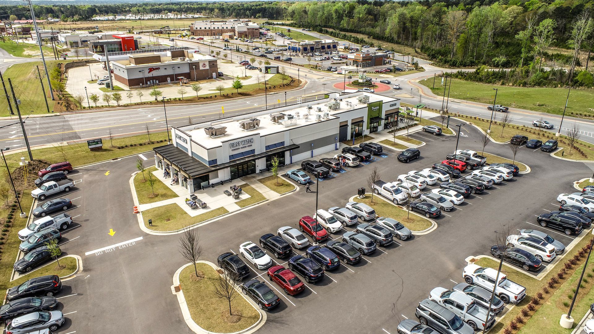 Aerial view of a modern commercial building with parking lots full of cars and trees around it