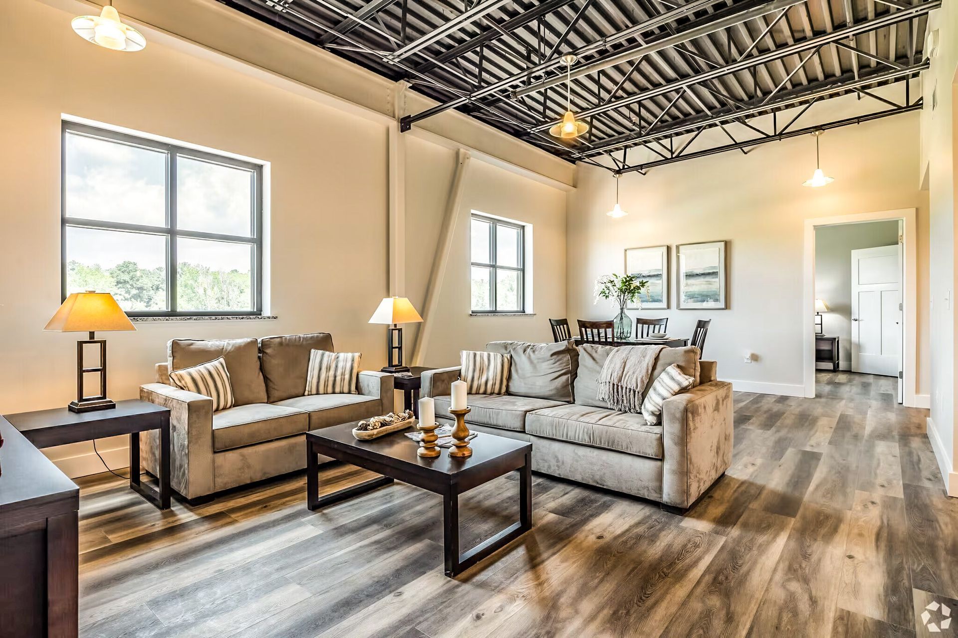 Bright living room with beige sofas, coffee table, wood floors, and large windows under an open ceiling