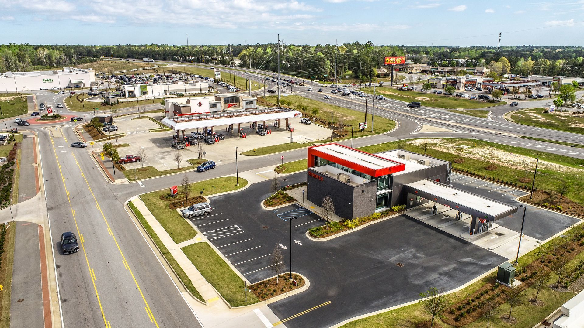 Aerial view of a gas station with a red roof beside a road and parking lot in a suburban area