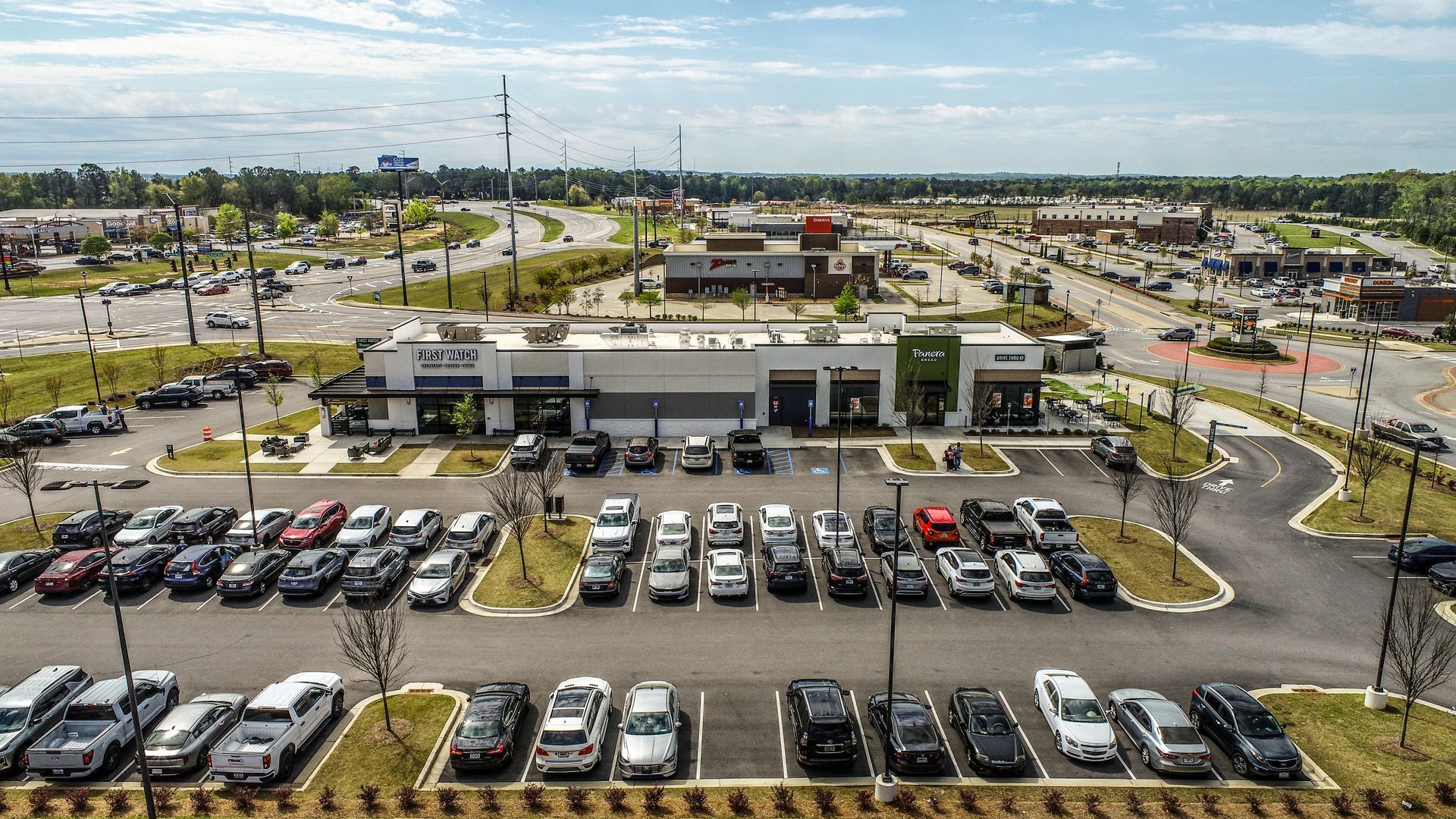 Aerial view of a large car dealership lot with rows of parked cars and surrounding roads.