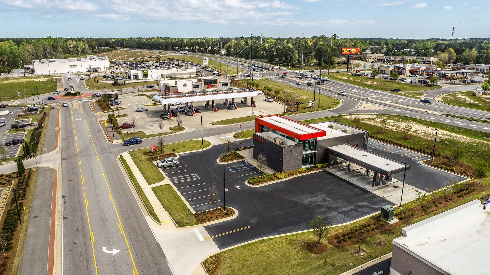 Aerial view of a gas station and convenience store beside a wide road and commercial area.