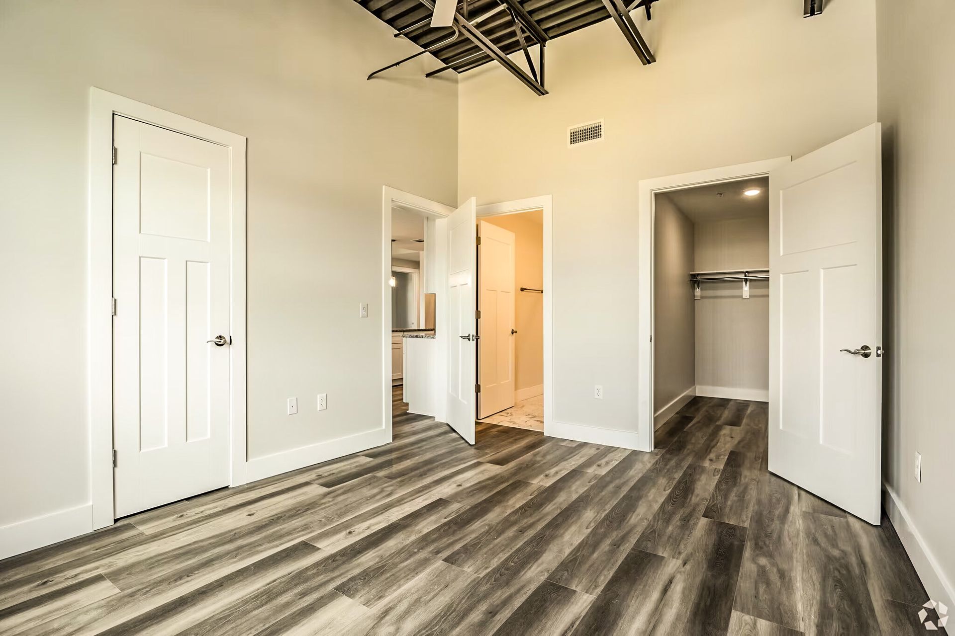 Empty modern bedroom with open closet doors, white walls, and gray wood-look flooring