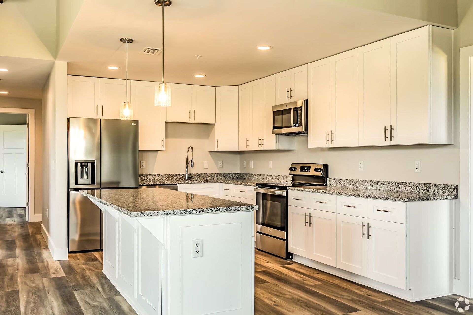 Bright modern kitchen with white cabinets, granite island, stainless steel appliances, and wood-look floors