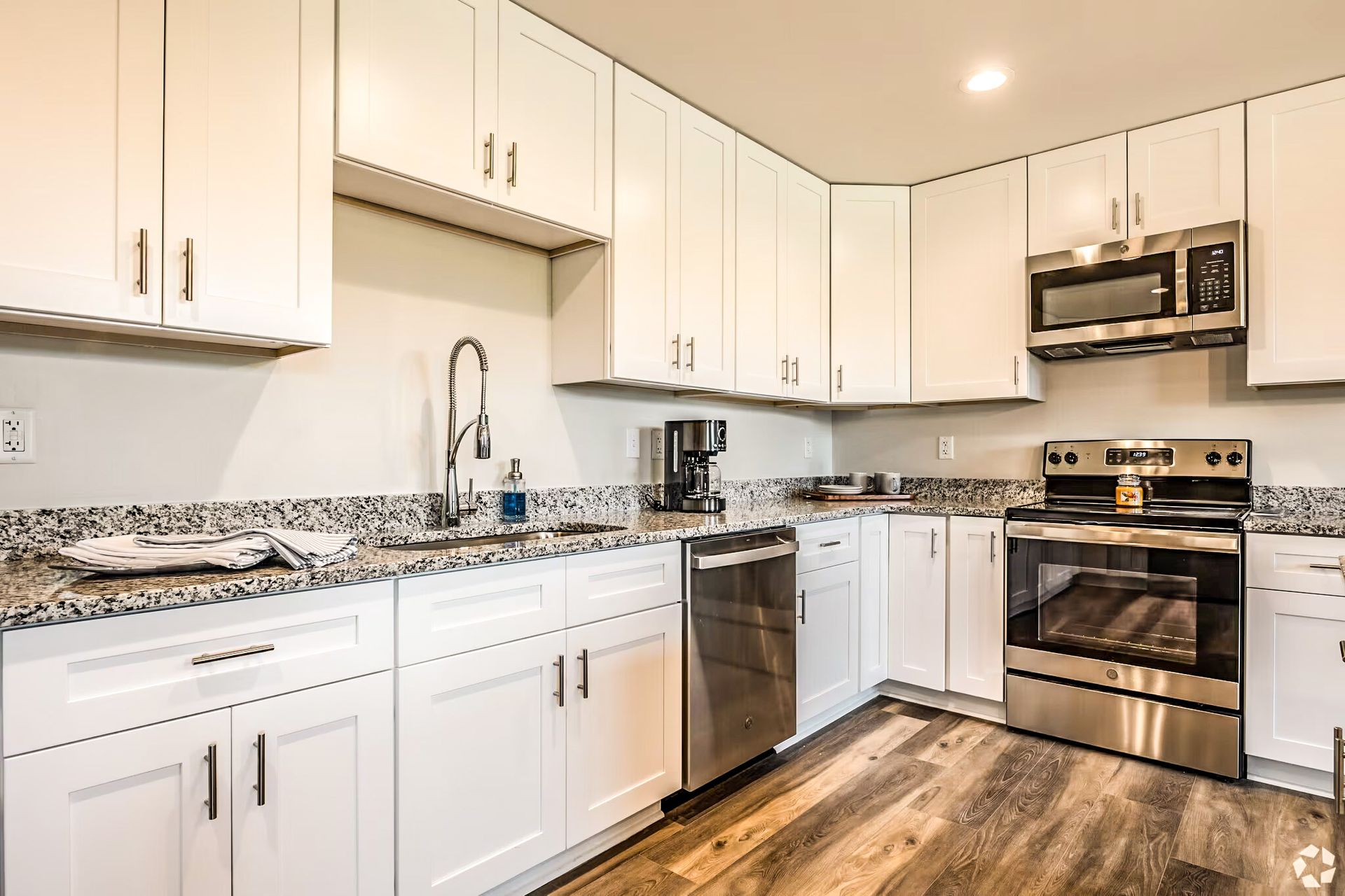 Bright modern kitchen with white cabinets, granite counters, stainless appliances, and wood floors