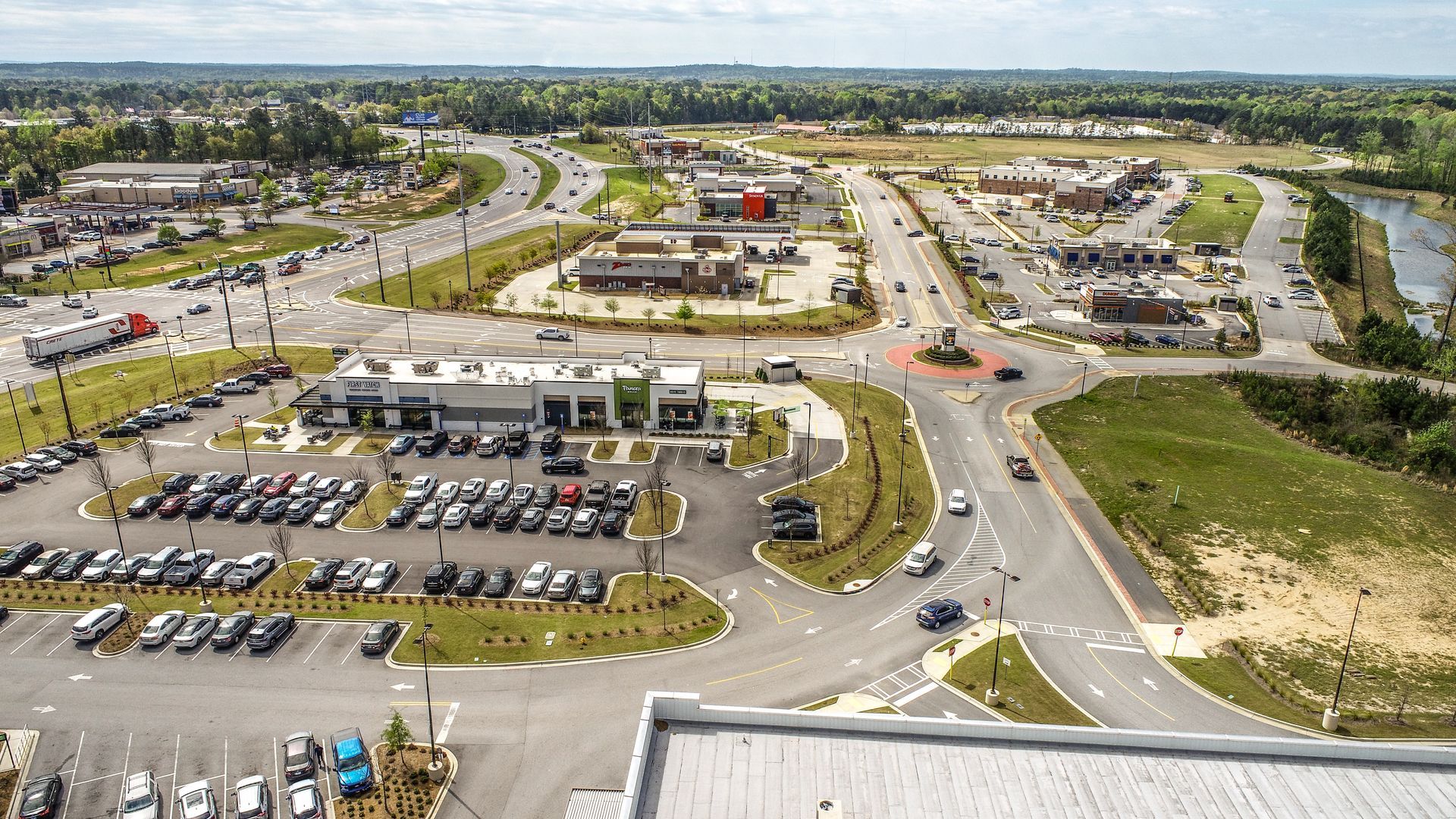 Aerial view of a suburban shopping center, parking lots, roads, and nearby green space.