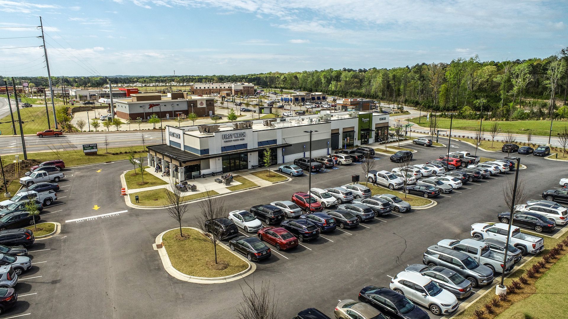 Aerial view of a modern apartment complex with a large parking lot and surrounding trees.