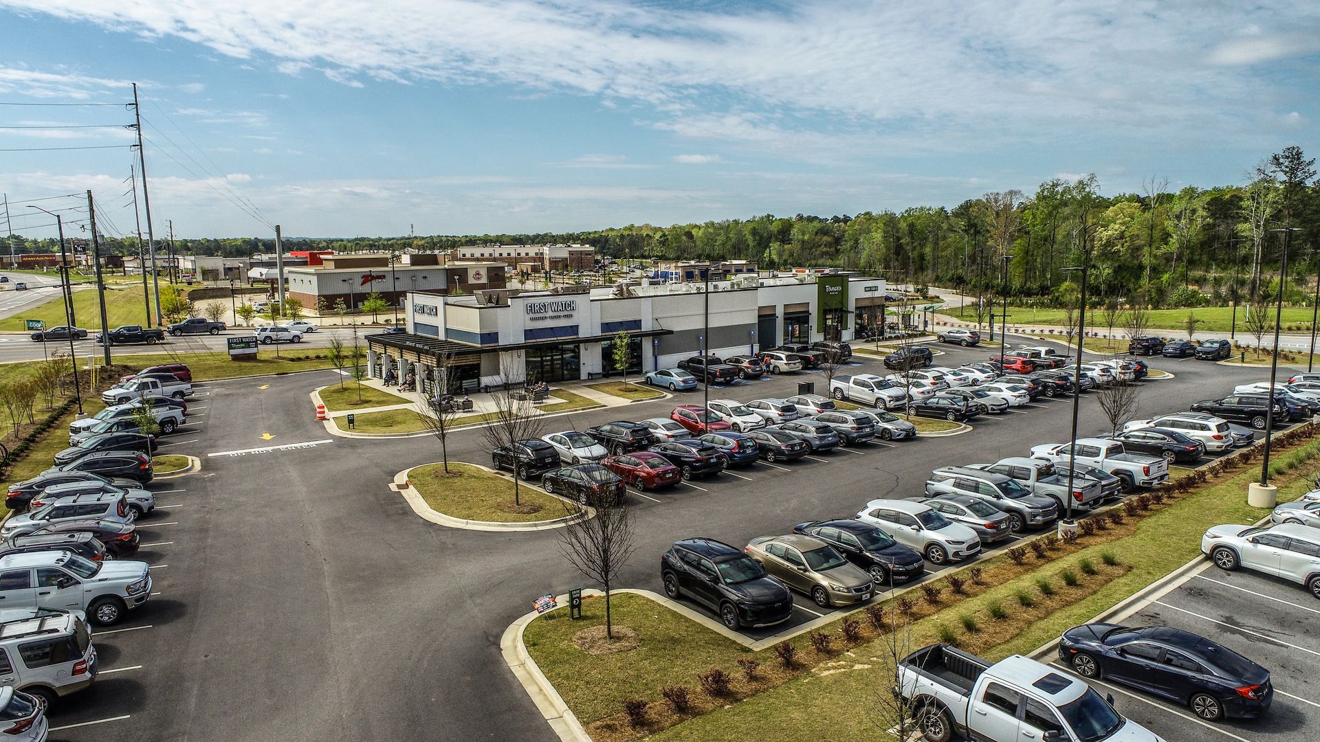 Aerial view of a modern office complex with a large parking lot full of cars on a sunny day