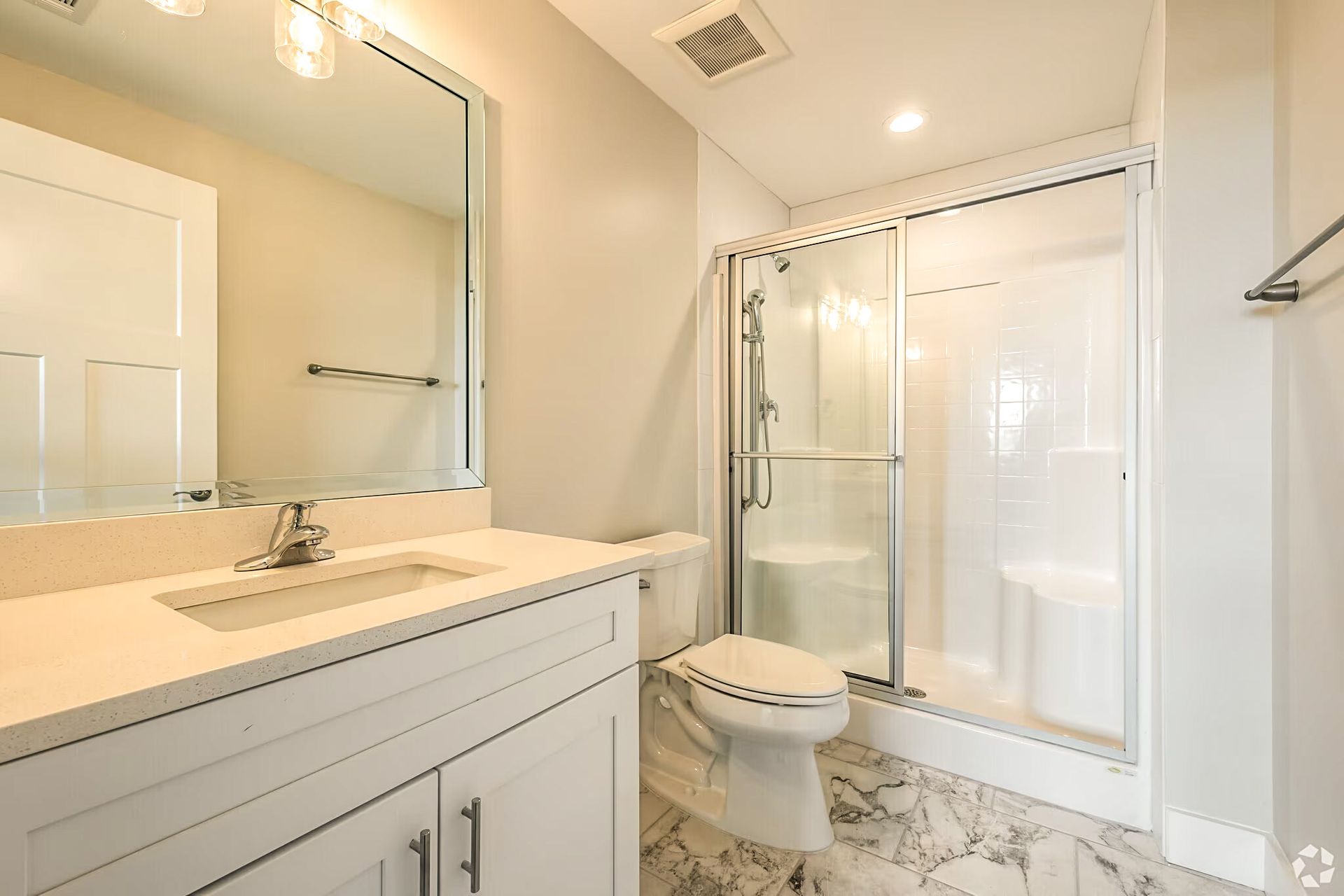 Bright bathroom with vanity mirror, sink, toilet, and glass-enclosed shower over marble tile floor