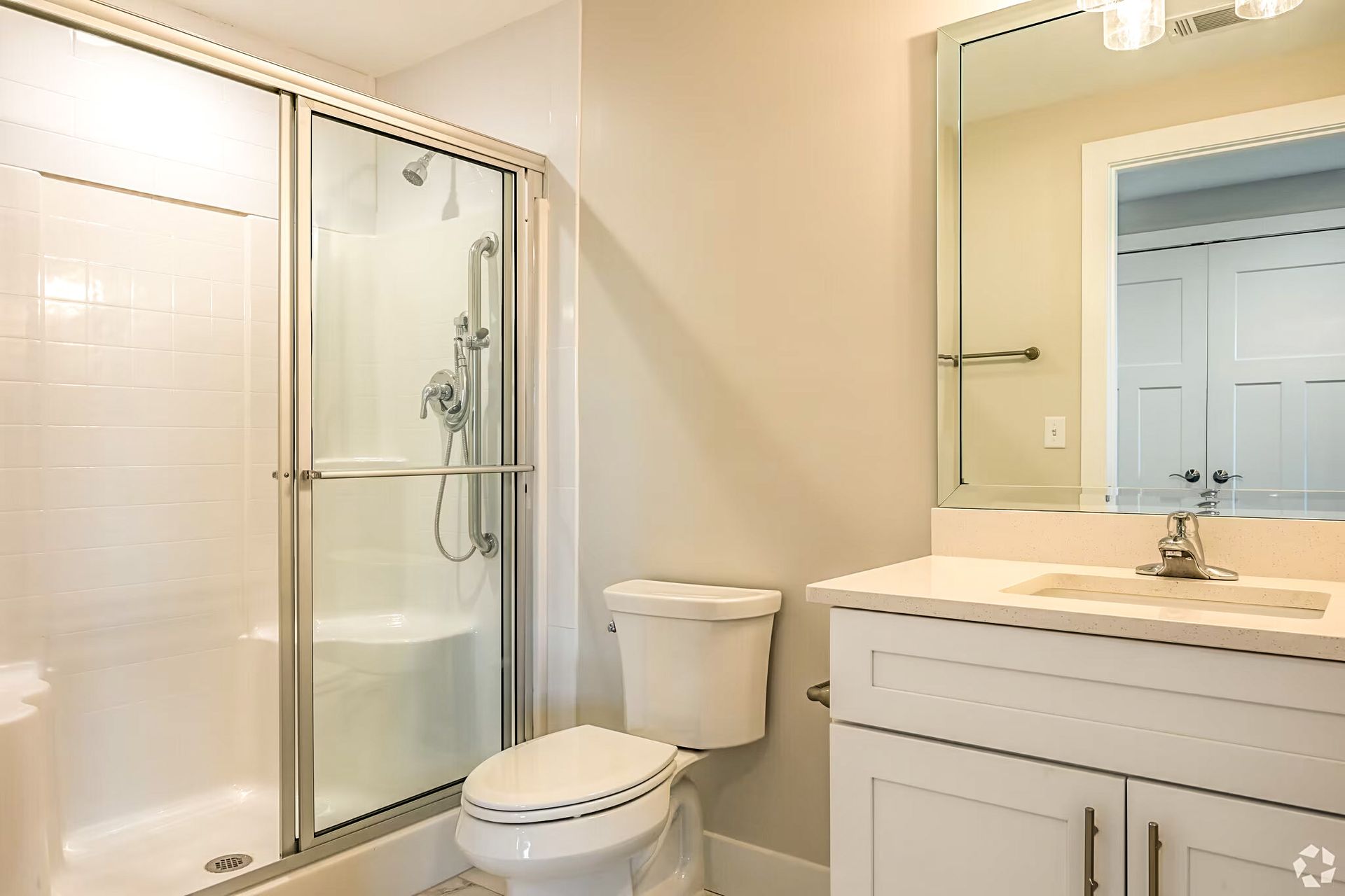 Bright bathroom with glass shower, toilet, and white vanity with mirror