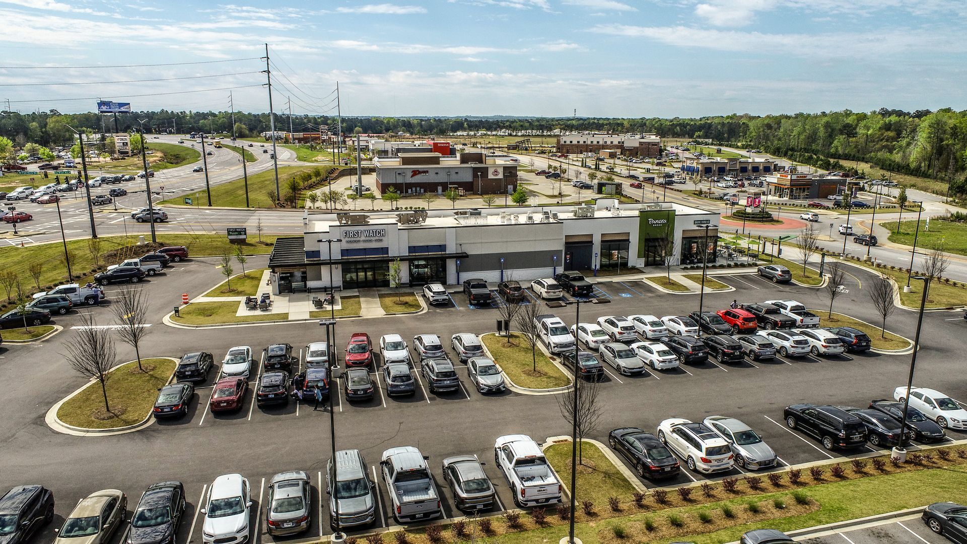 Aerial view of a busy shopping center parking lot with many cars and a low commercial building