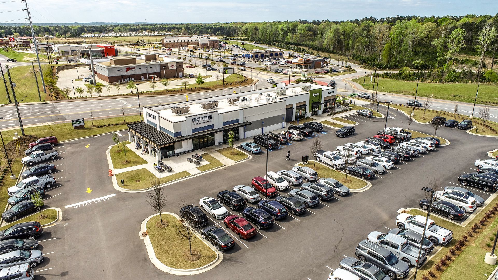 Aerial view of a modern office building with a large parking lot and surrounding trees
