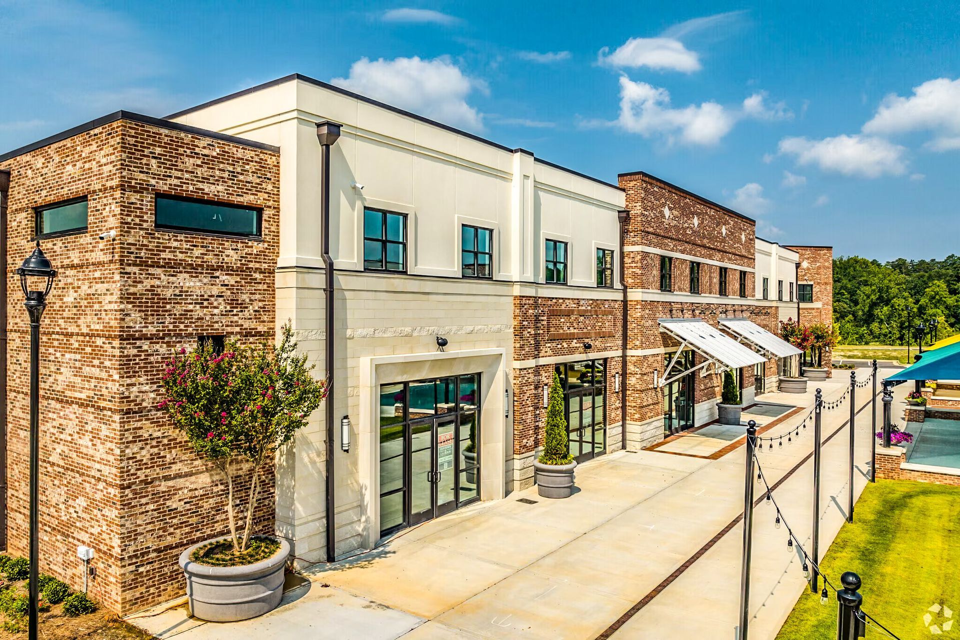 Modern brick-and-white storefronts with large windows and awnings along a sunny sidewalk