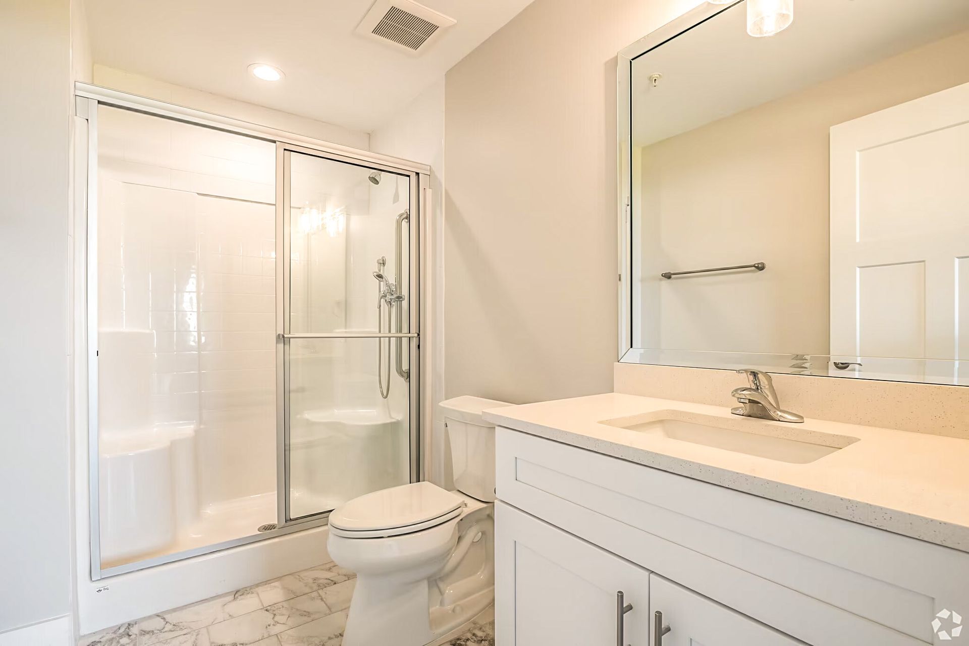 Bright white bathroom with glass shower, toilet, and vanity mirror