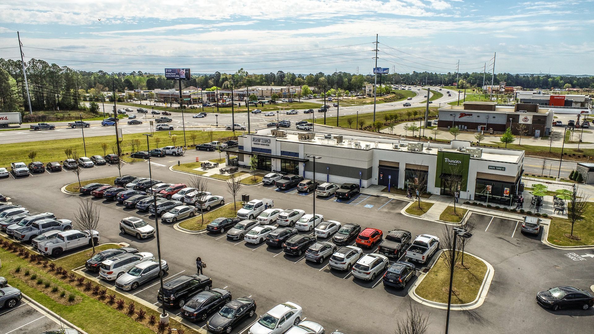 Aerial view of a car dealership lot with rows of parked vehicles and a white showroom building
