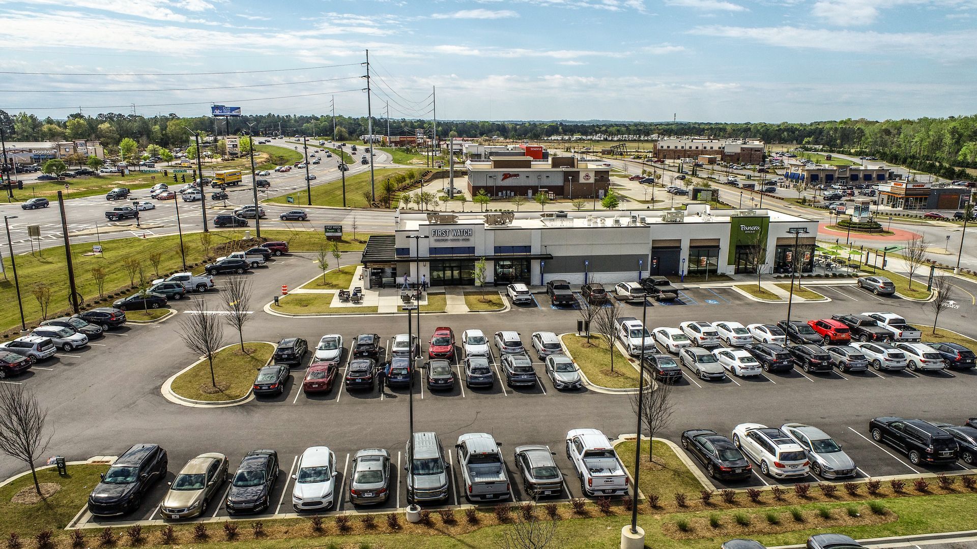 Aerial view of a busy parking lot and shopping plaza on a sunny day