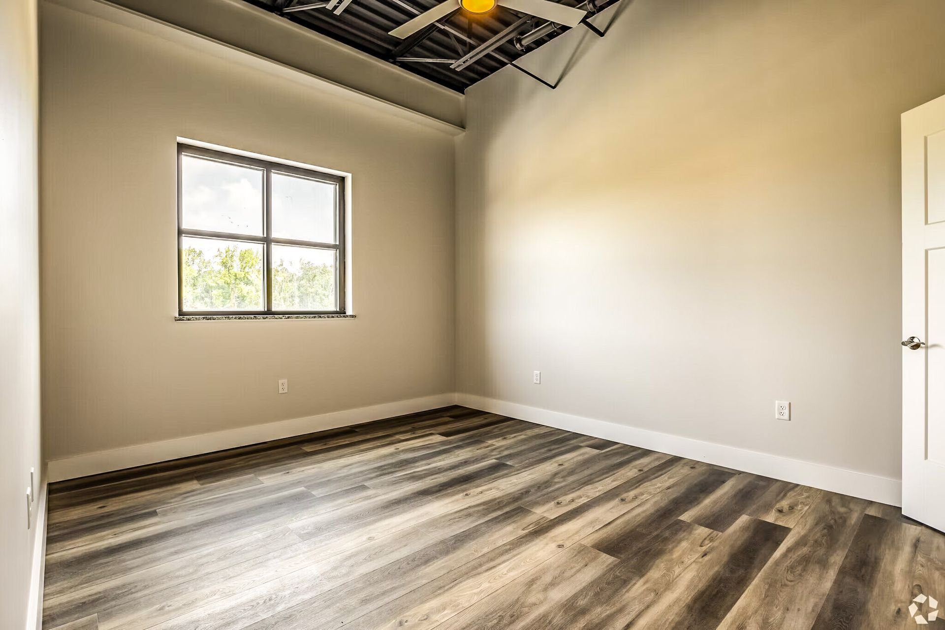 Empty room with gray walls, wood-look floor, window, and exposed ceiling beams