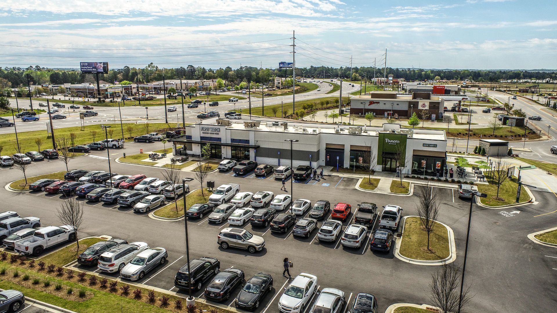 Aerial view of a large car dealership with rows of parked cars and a showroom under a clear sky.