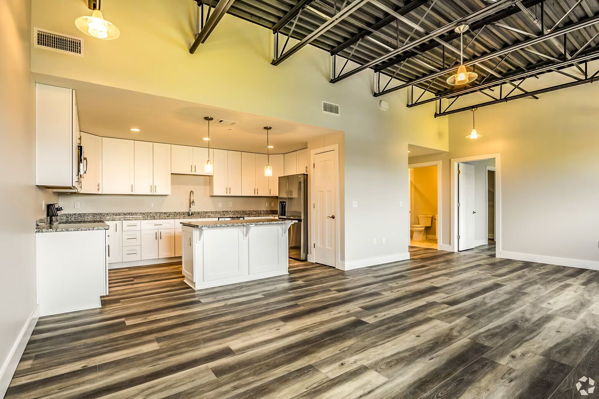 Spacious open-concept kitchen and living area with white cabinets, wood floors, and exposed ceiling beams