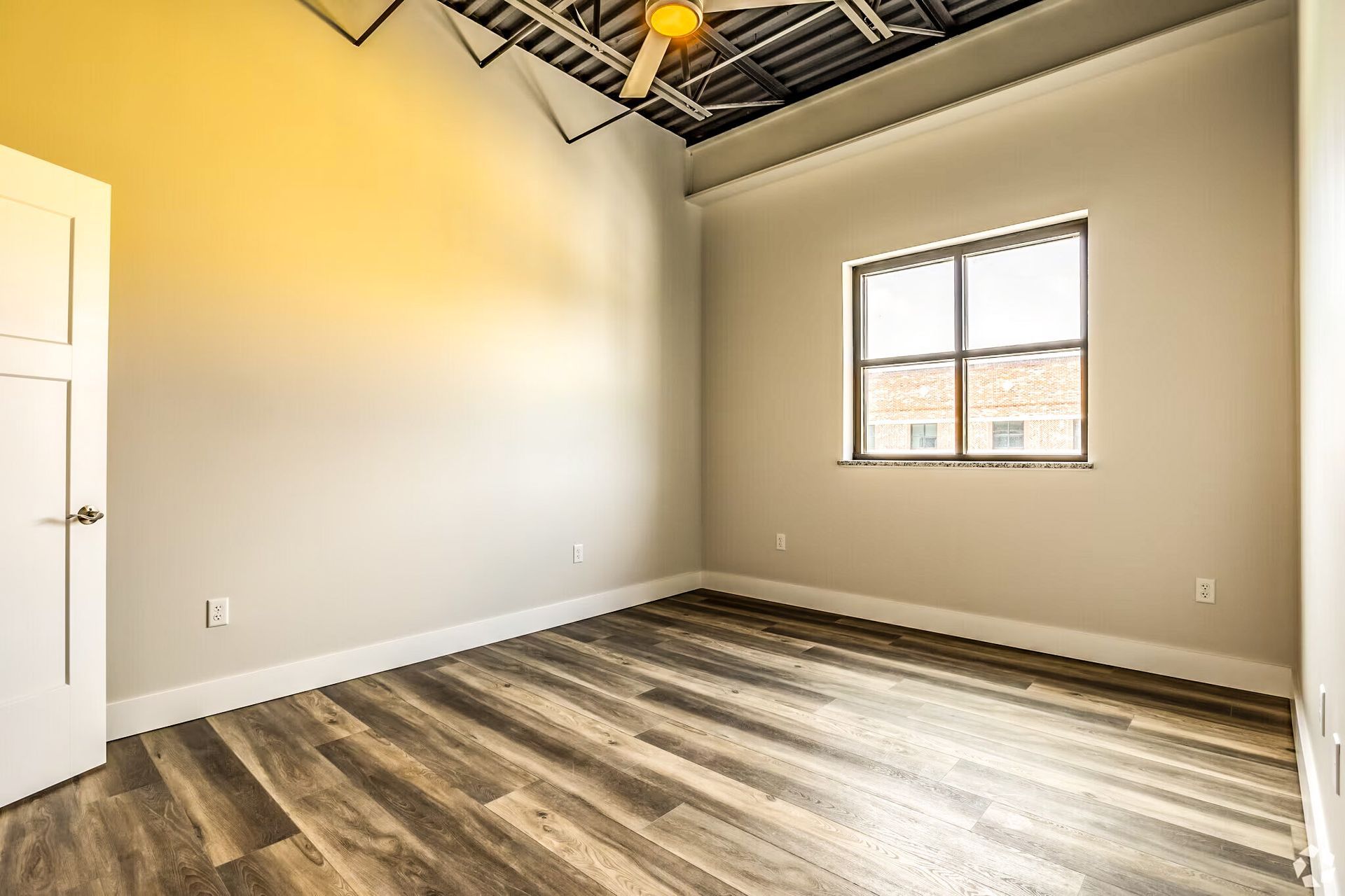 Empty room with gray wood-look floors, beige walls, and a small window.