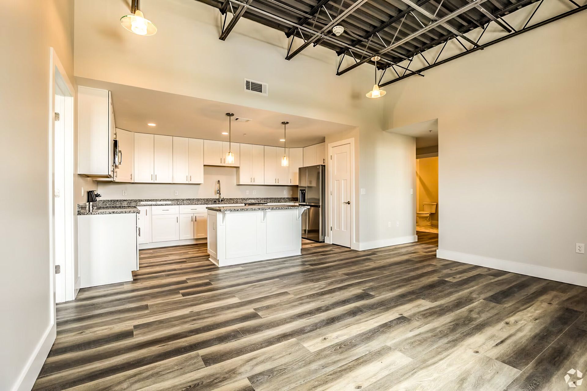 Open-concept kitchen and living area with white cabinets, wood-look floors, and exposed ceiling beams