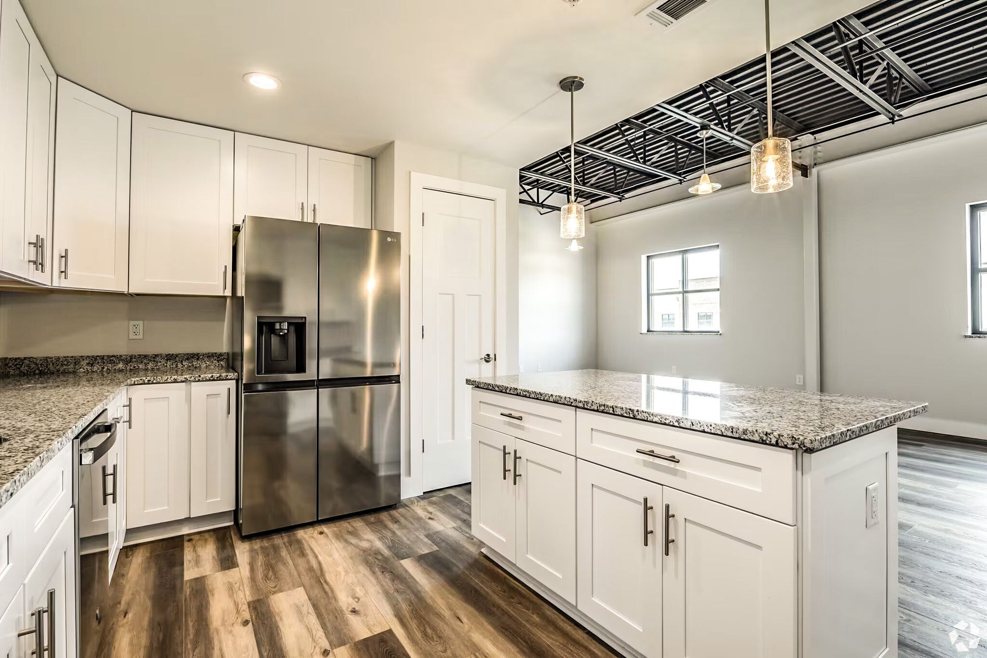 Bright modern kitchen with white cabinets, stainless steel fridge, granite island, and wood floors