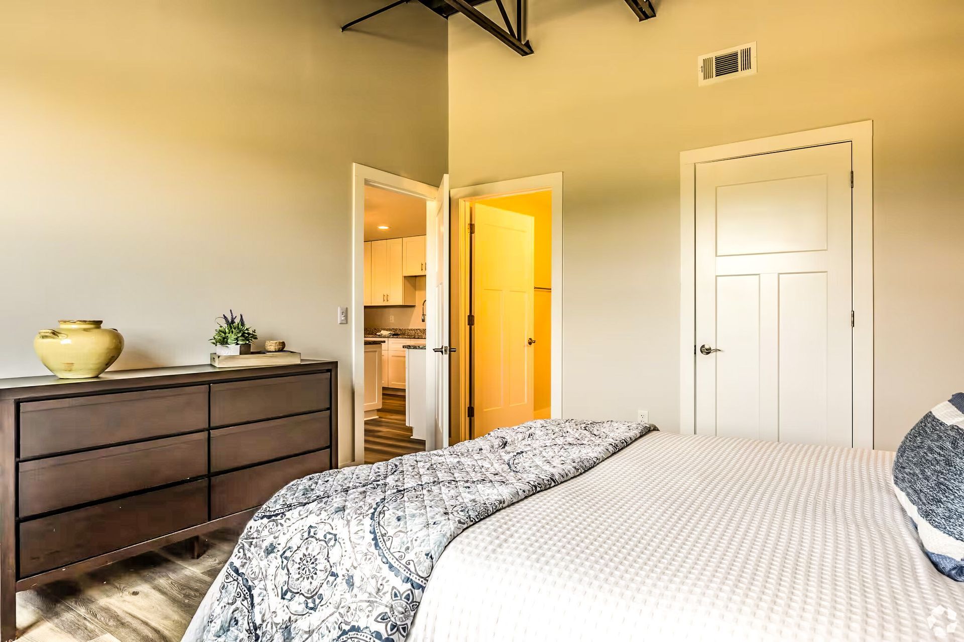 Bright bedroom with bed, dresser, open doors, and soft yellow lighting