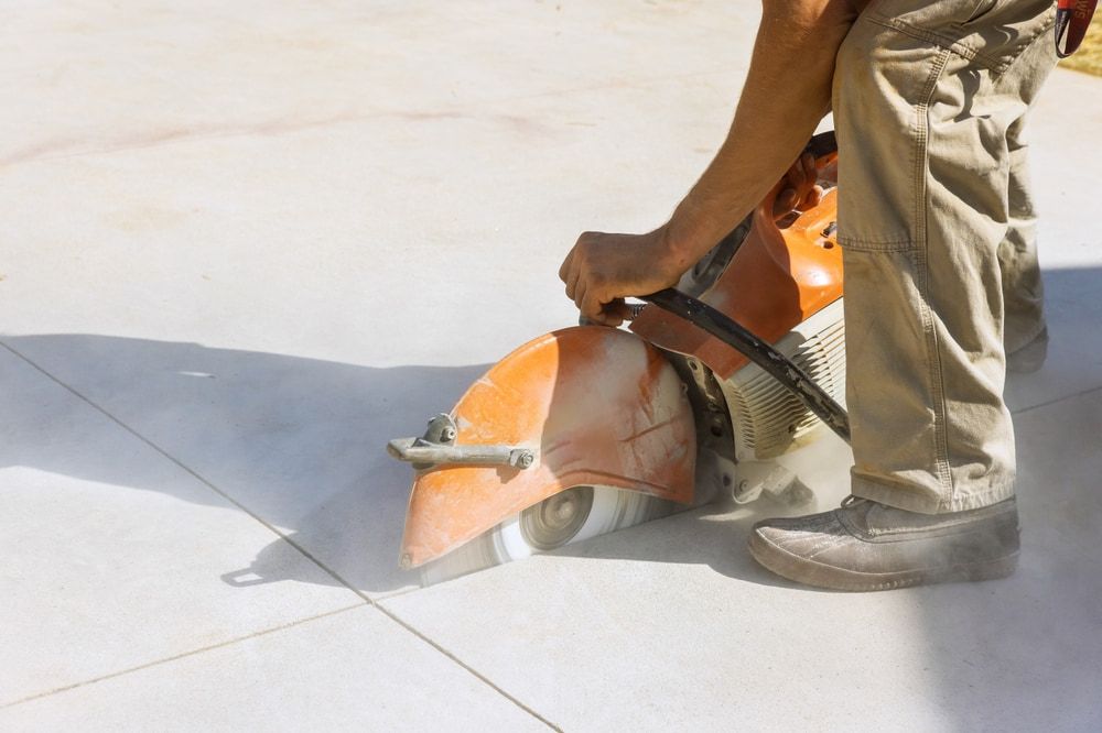 A Man Is Using A Concrete Saw To Cut A Concrete Driveway — Chad Taylor Plumbing In Forster, NSW