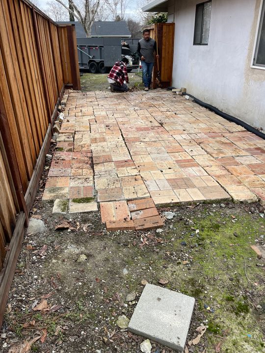 A man is standing on a brick patio in front of a house.