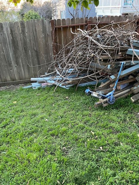 A pile of wood is sitting on top of a lush green lawn next to a wooden fence.