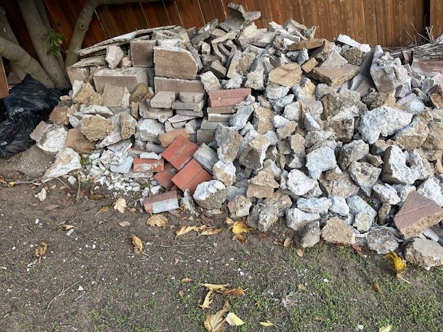 A pile of rocks and bricks is sitting on the ground in front of a wooden fence.