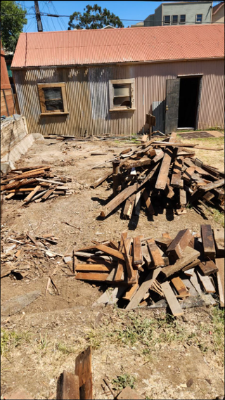 A pile of wood in front of a building with a red roof