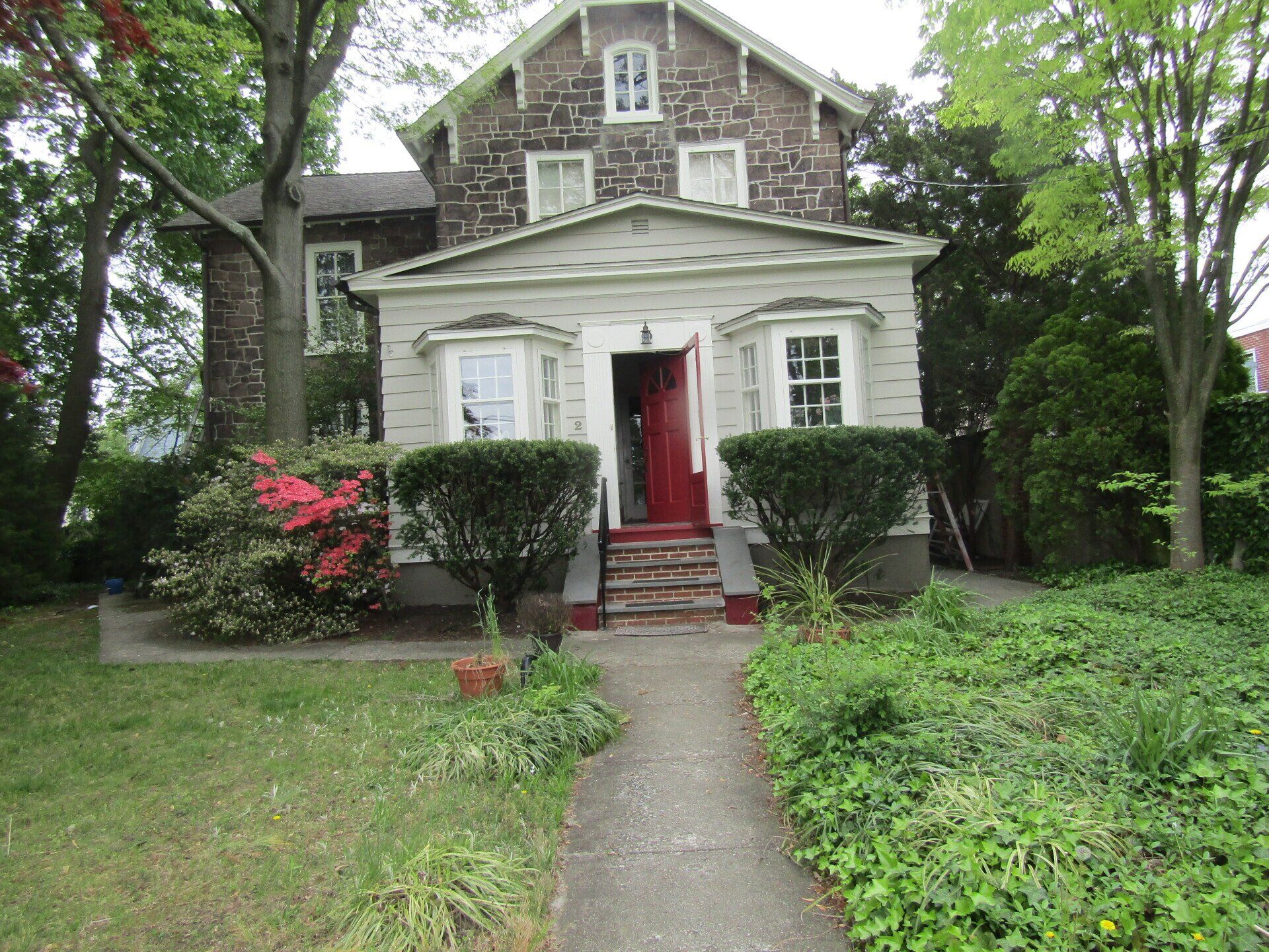 A large stone house with a red door is surrounded by trees and bushes