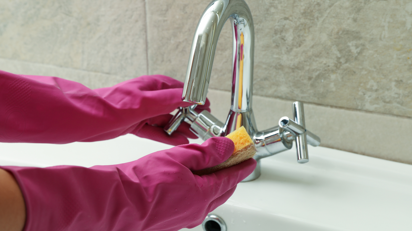 a person wearing pink rubber gloves is cleaning a faucet with a brush .