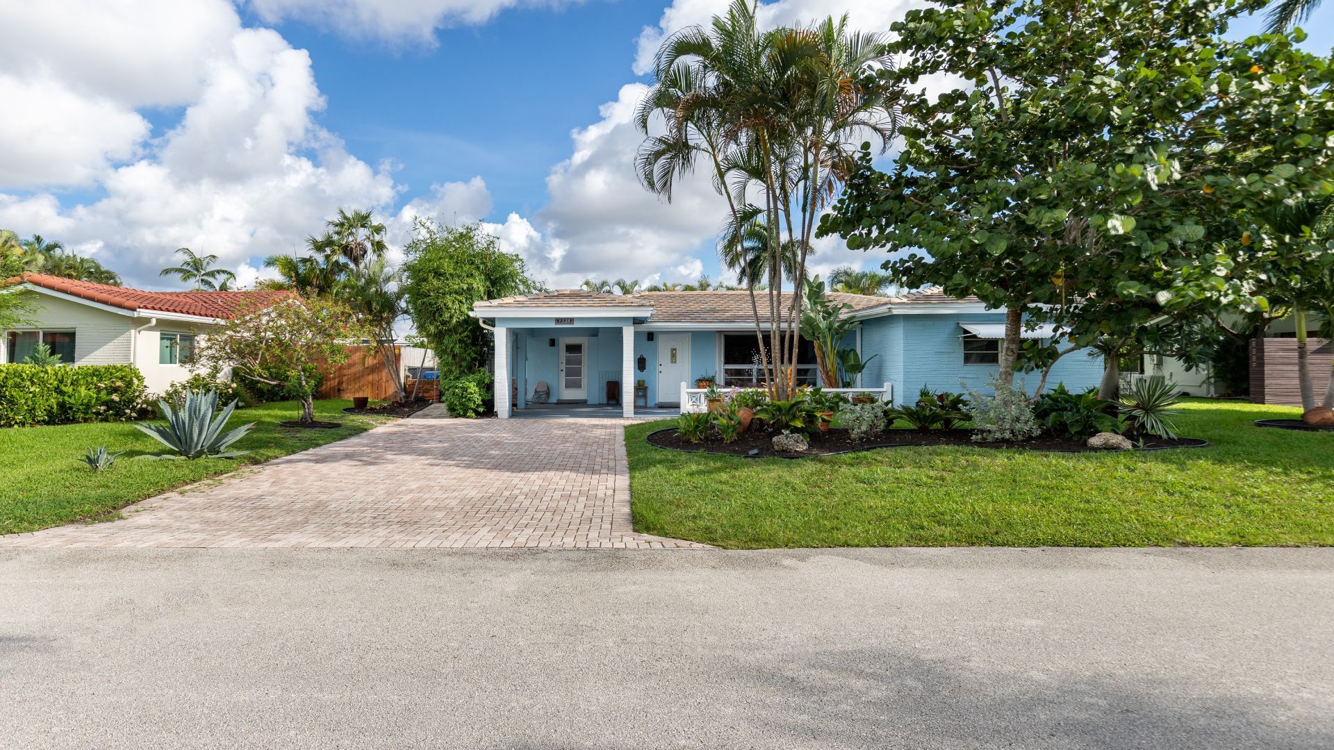 A blue house with a driveway and trees in front of it