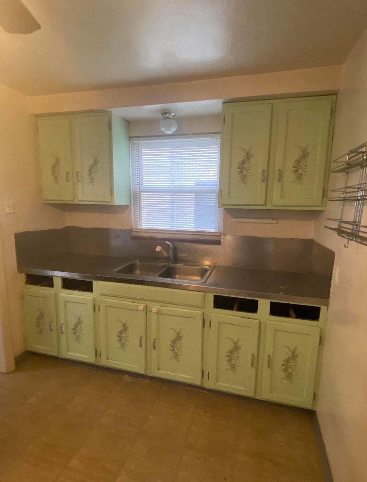 An empty kitchen with green cabinets and a sink.