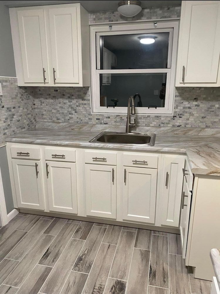 A kitchen with white cabinets , a sink , and a window.