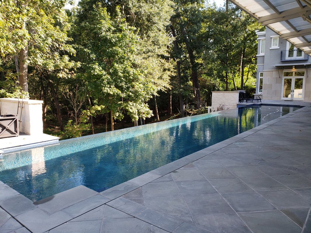 A large swimming pool is surrounded by trees and a house.