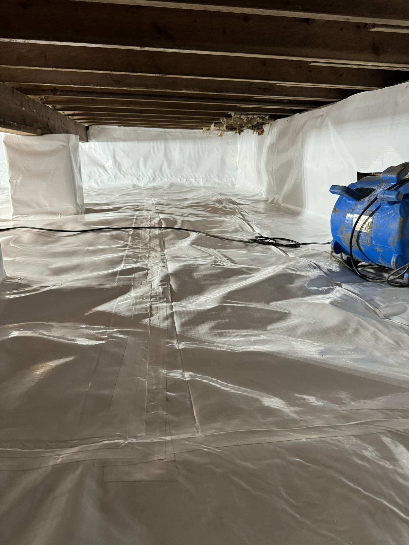 A blue air compressor is sitting on top of a plastic sheet in a basement.