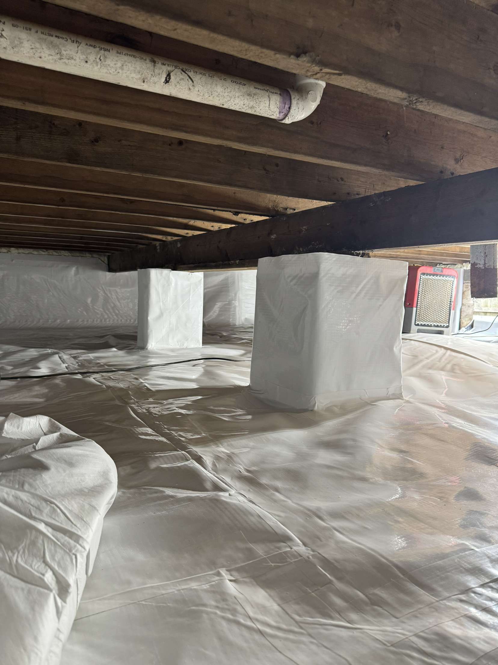 A basement with a lot of plastic covering the floor and pillars.