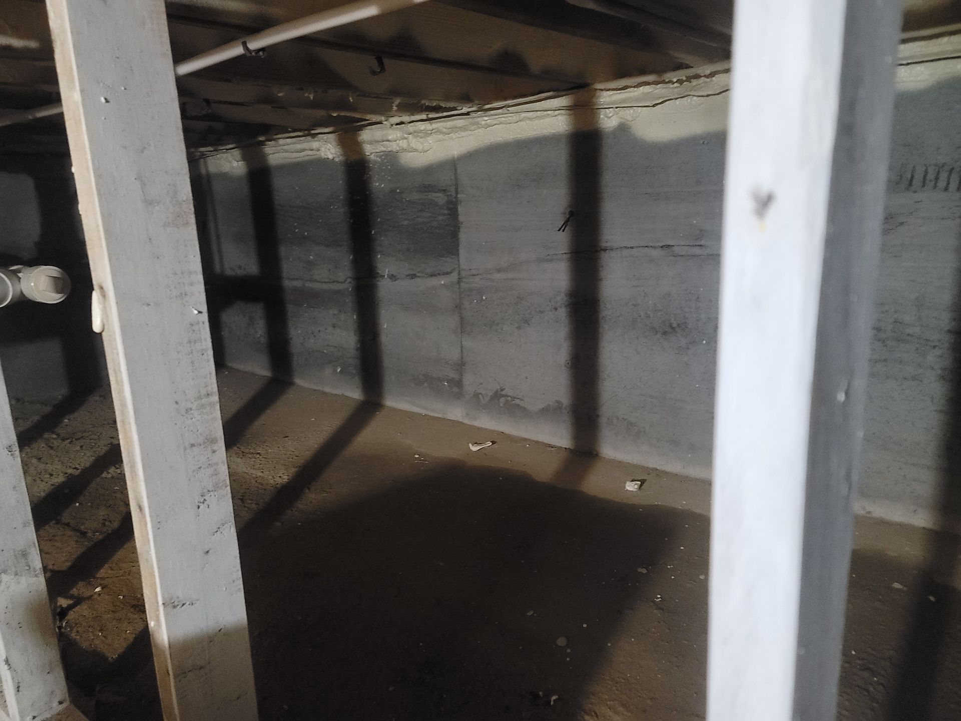 An empty basement with a concrete wall and wooden beams.