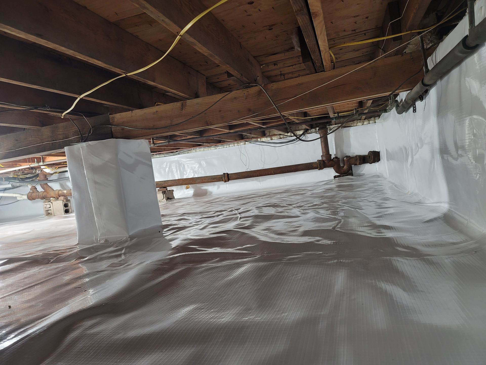 A crawl space under a house covered in plastic.