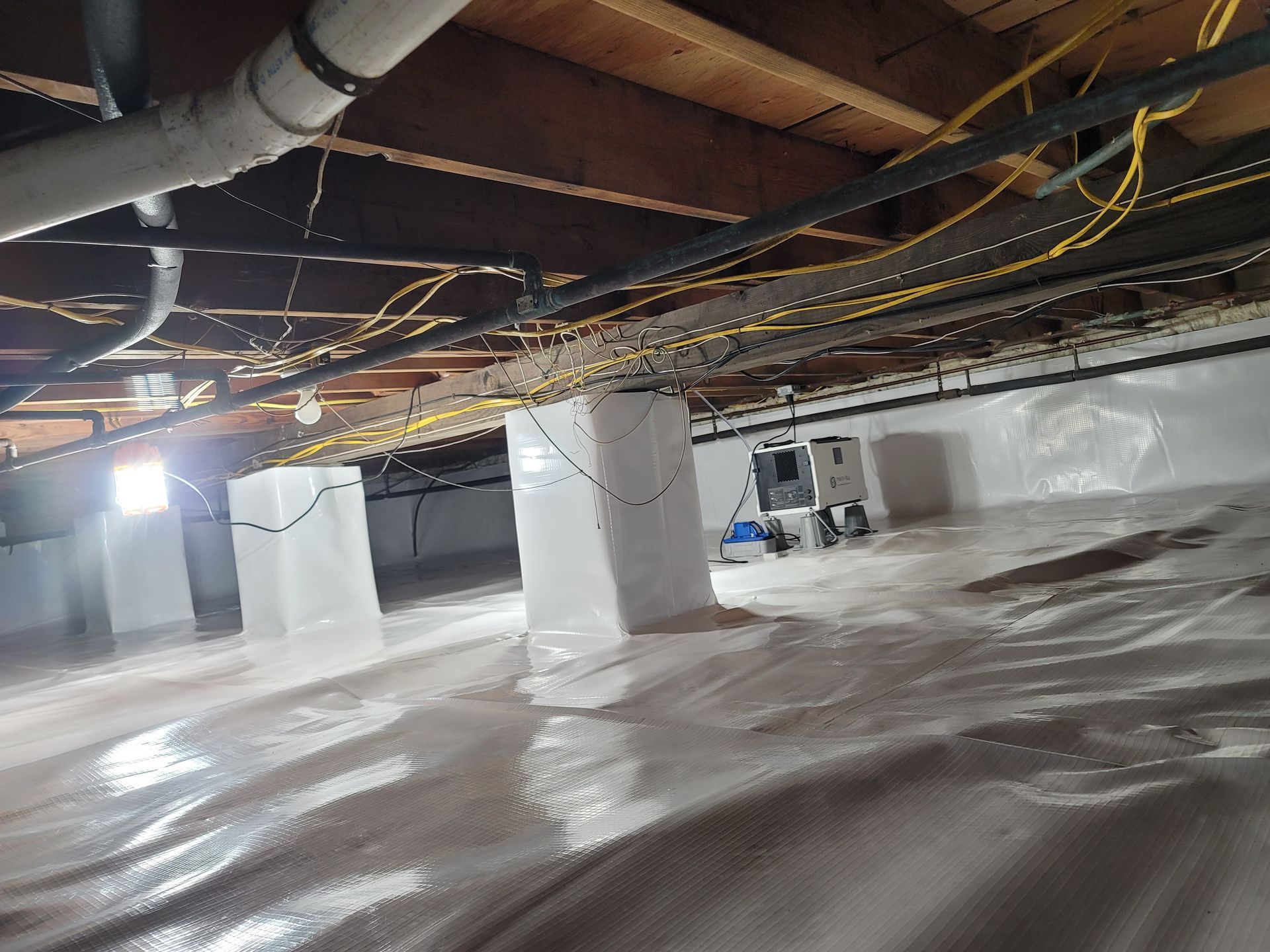 A basement with a lot of pipes and a lot of plastic on the floor.