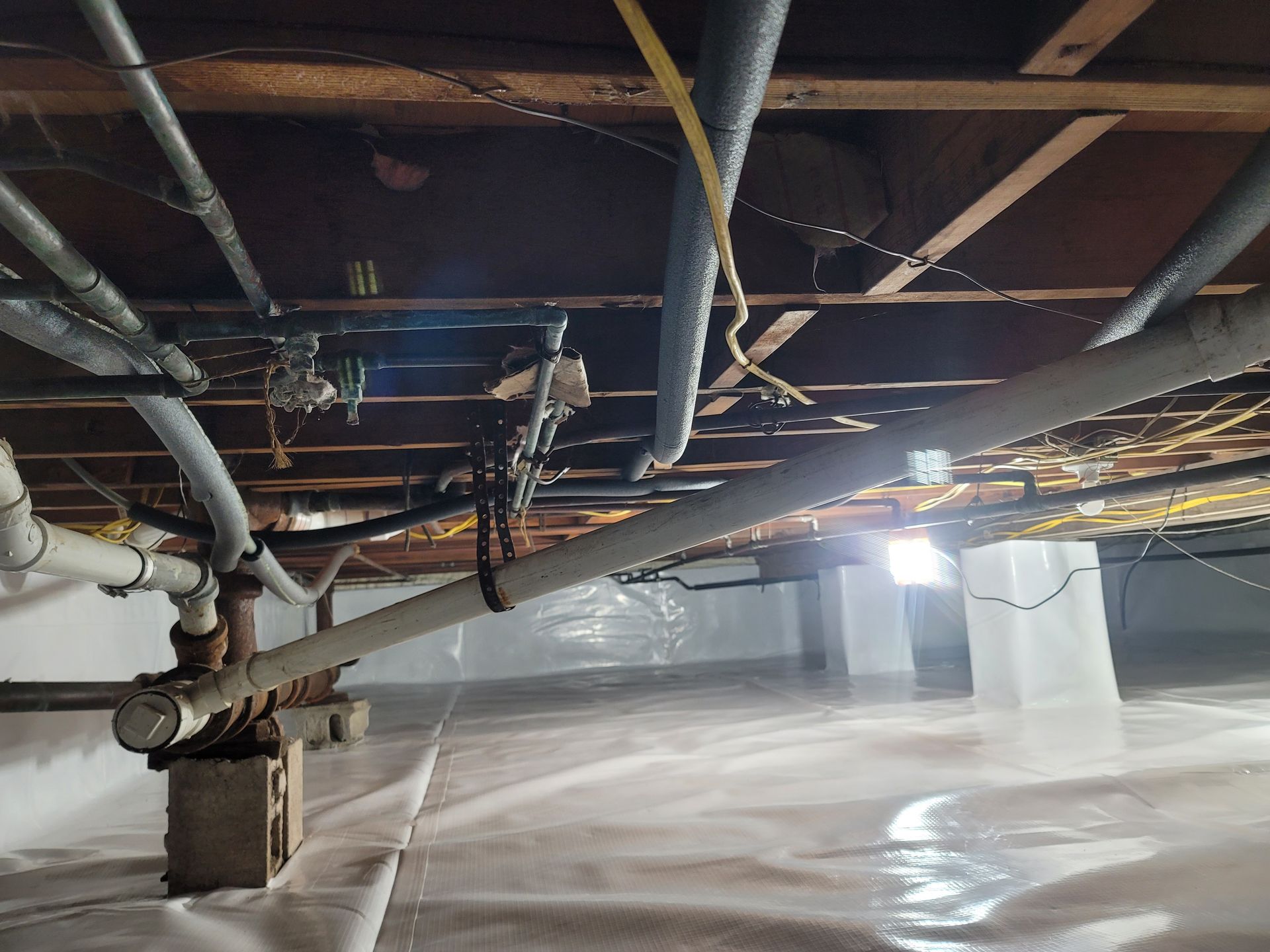A basement with a lot of pipes and wires hanging from the ceiling.