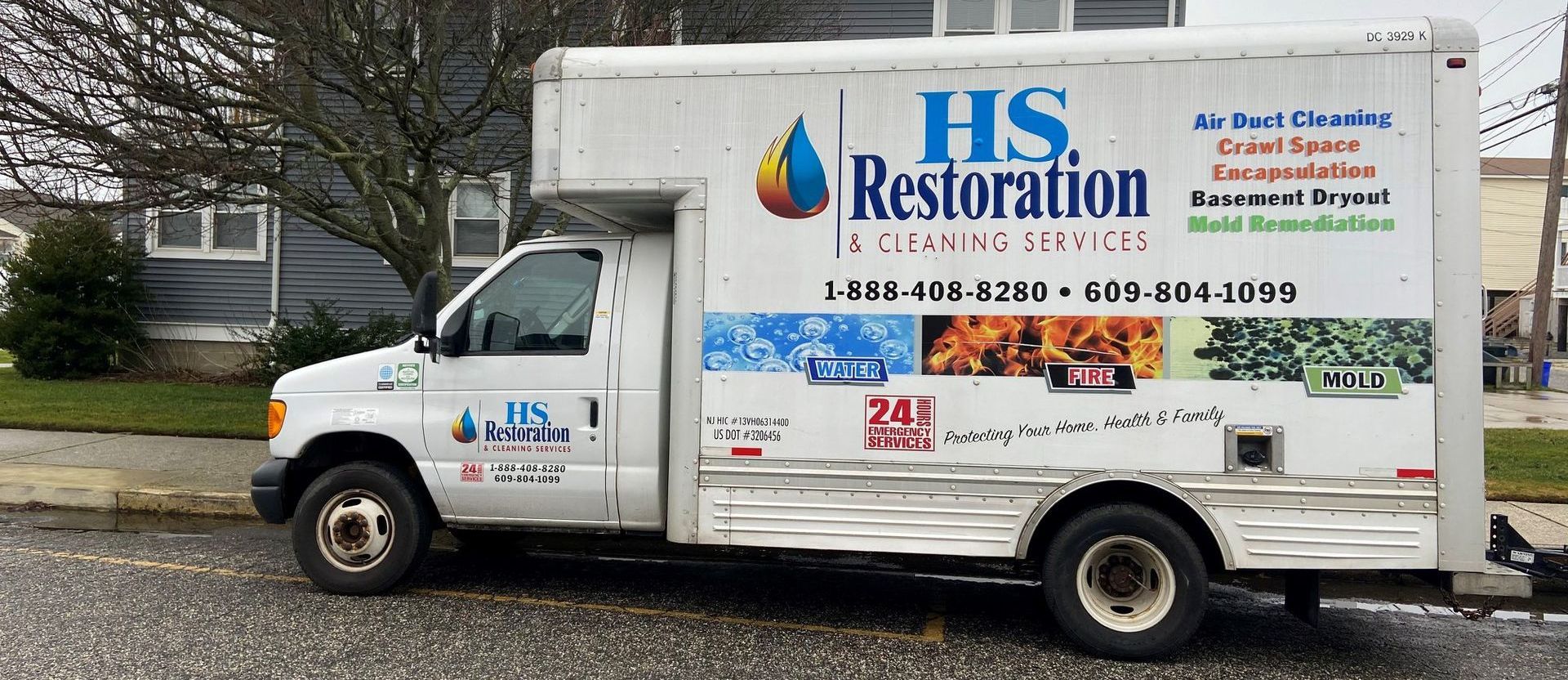 A white hs restoration truck is parked on the side of the road.