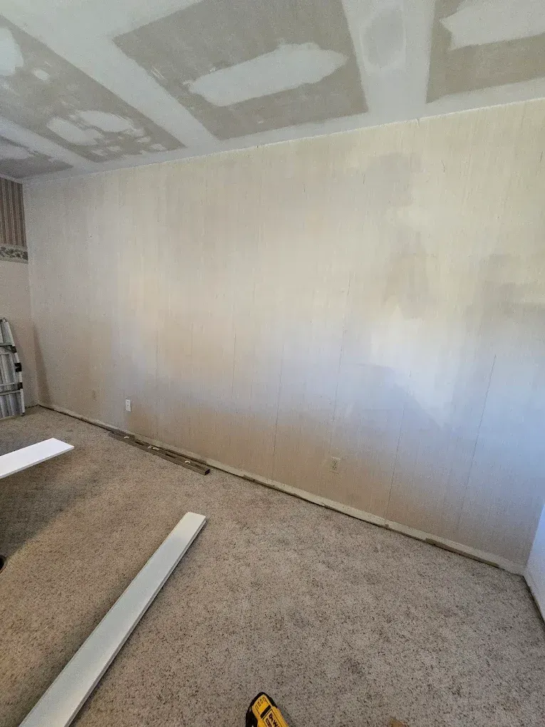 Partially finished room with drywall ceiling, beige wall, carpeted floor, and construction materials.