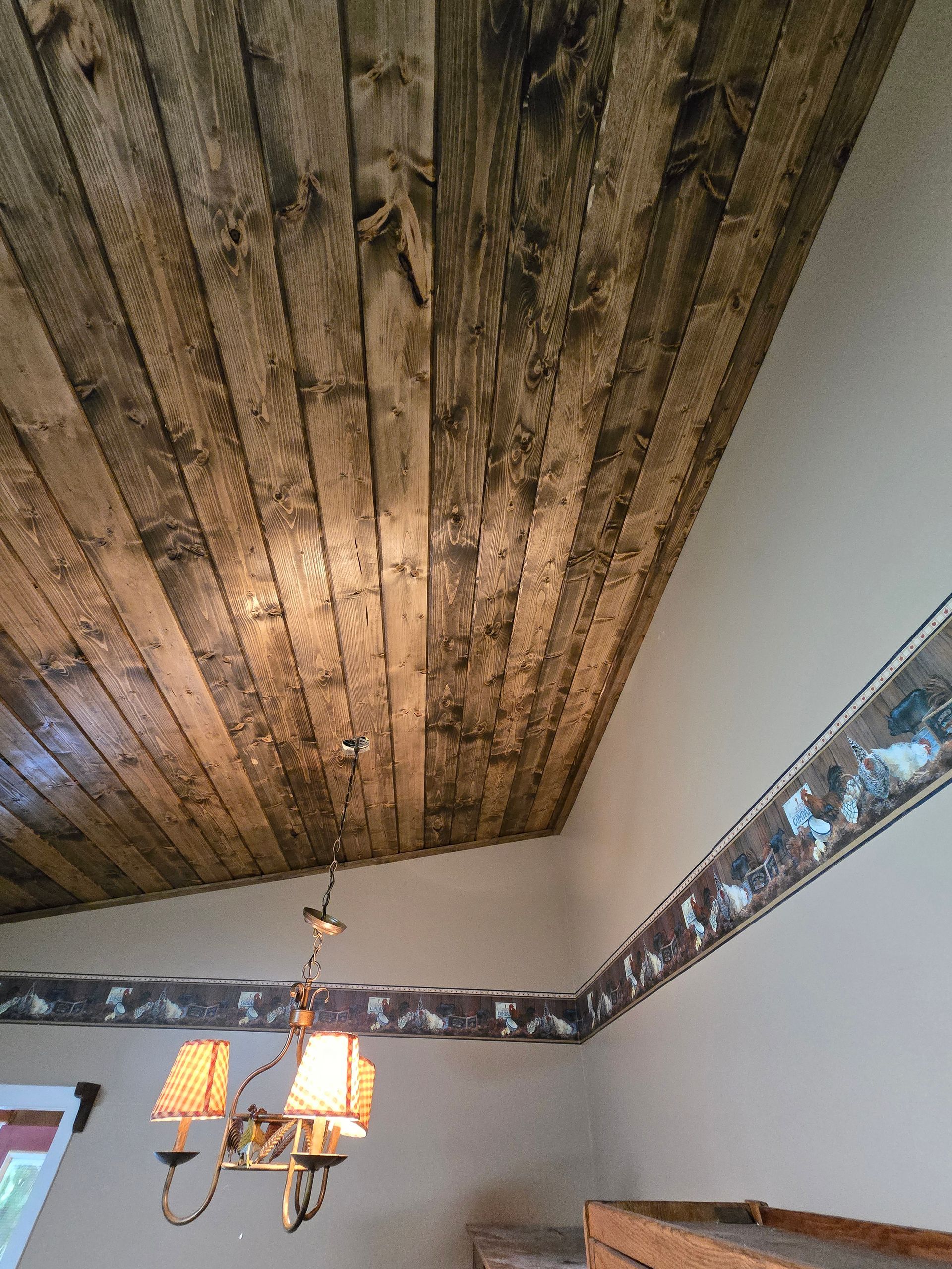 Rustic wood-plank ceiling with a hanging chandelier in a room with decorative wall trim