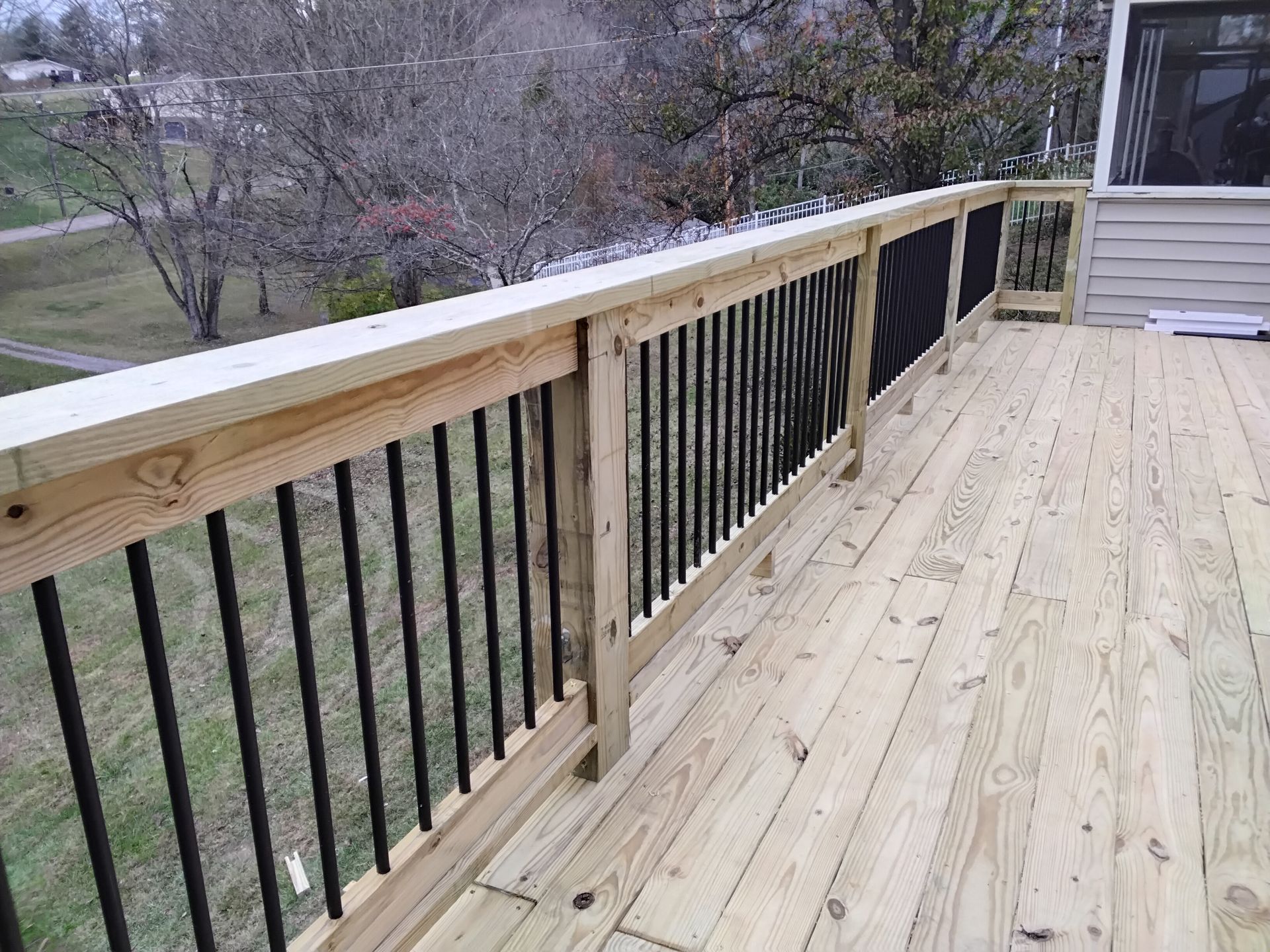 Wooden deck with black railings overlooking a backyard with bare trees